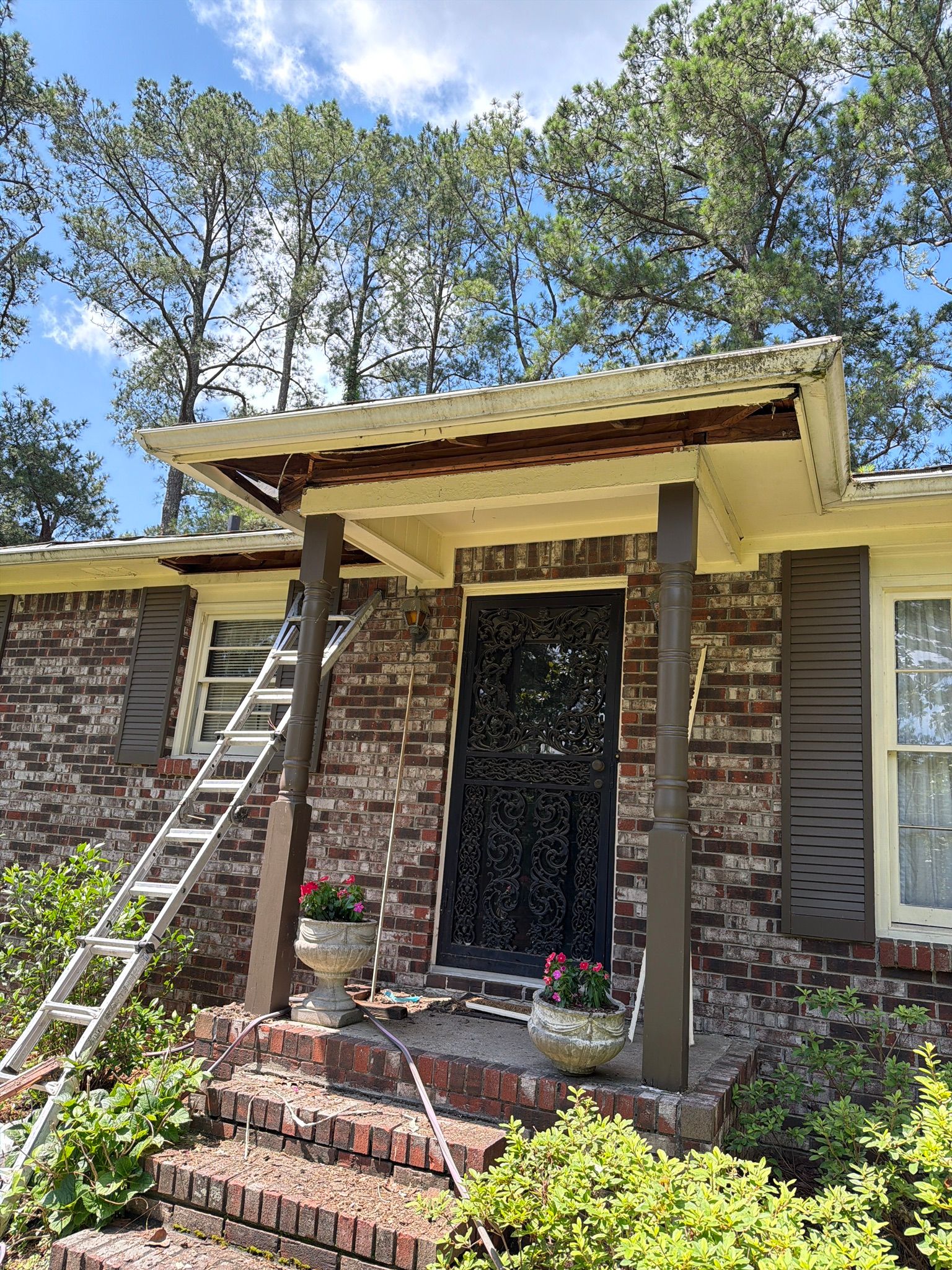 Exposed wood framing is visible along a front porch roofline during a fascia repair.
