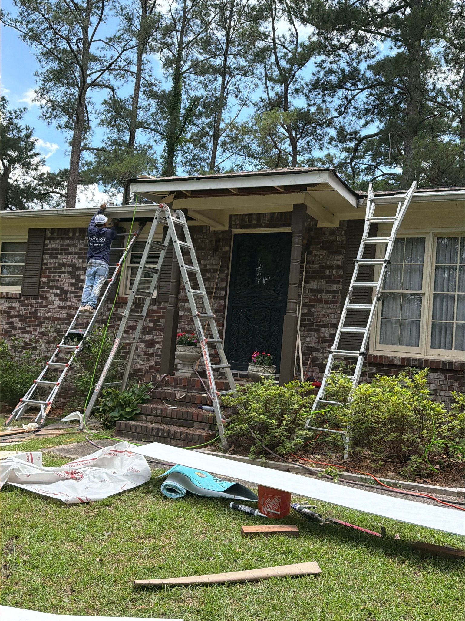 Replacement trim boards and roofing tools lie on the front lawn during a gutter repair job.