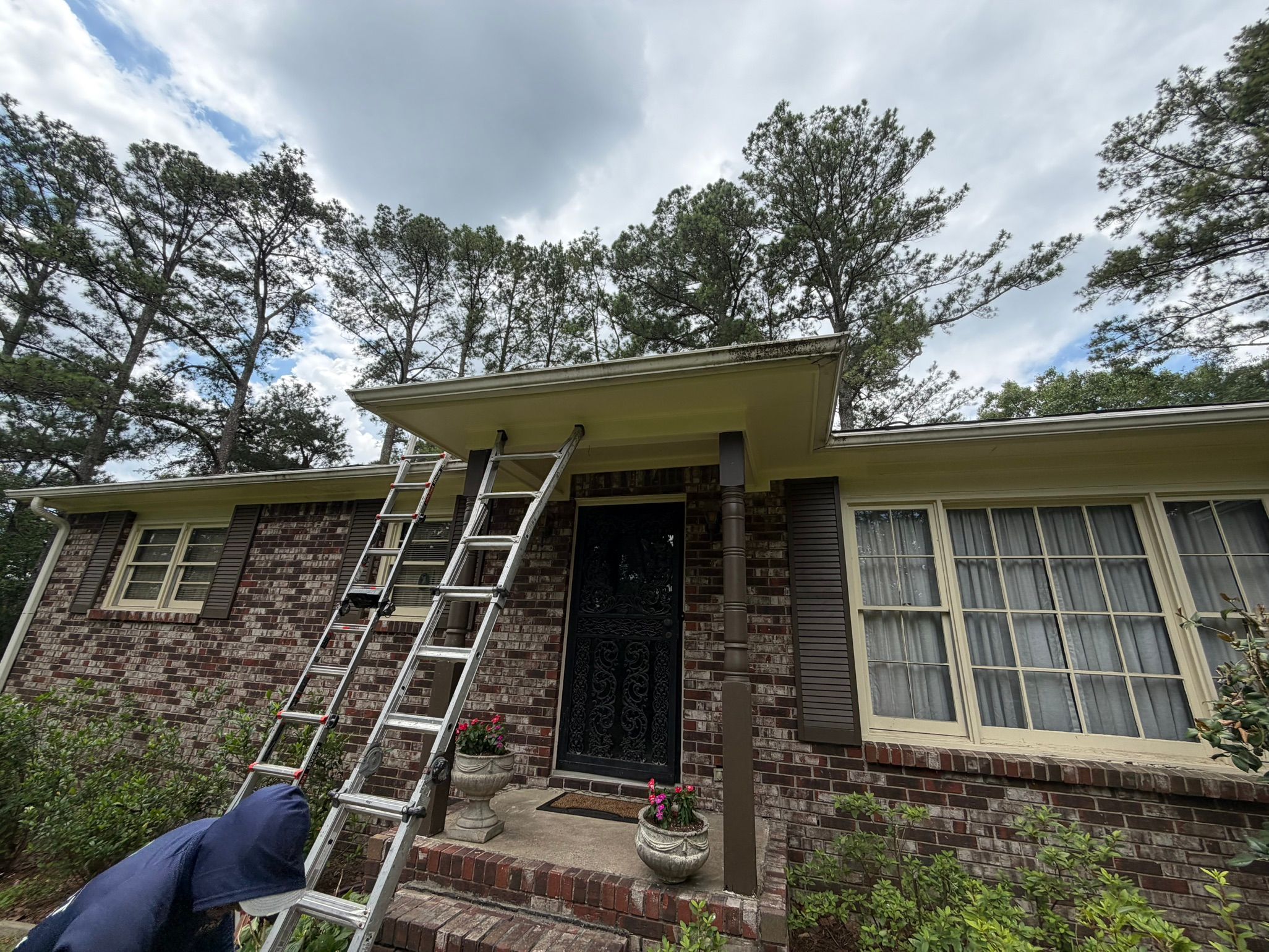 Two aluminum ladders lean against the porch roofline while repairs are made to the soffit.