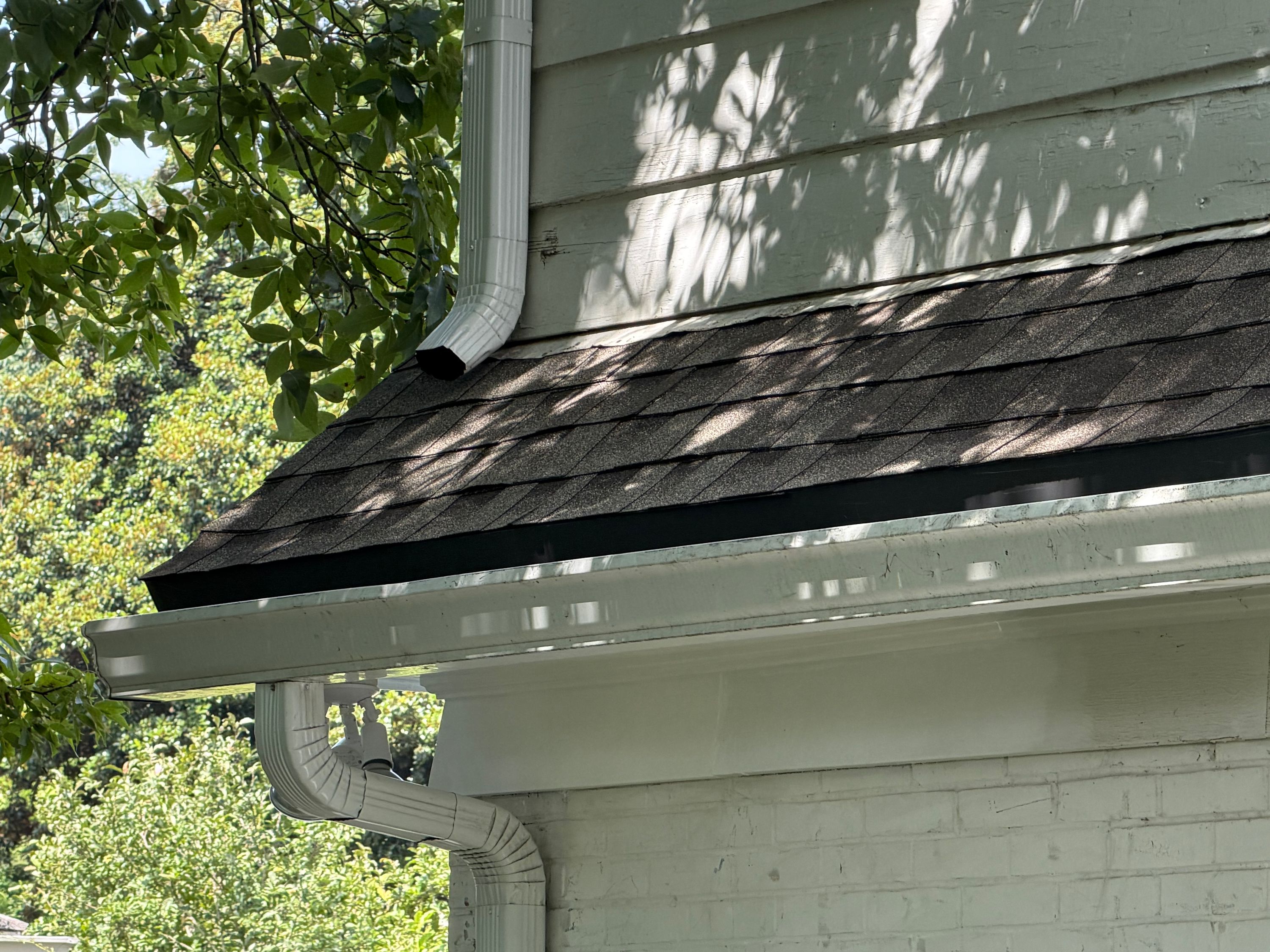 Dark asphalt shingles line the roof edge next to wood siding on a Brookwood Forest home.