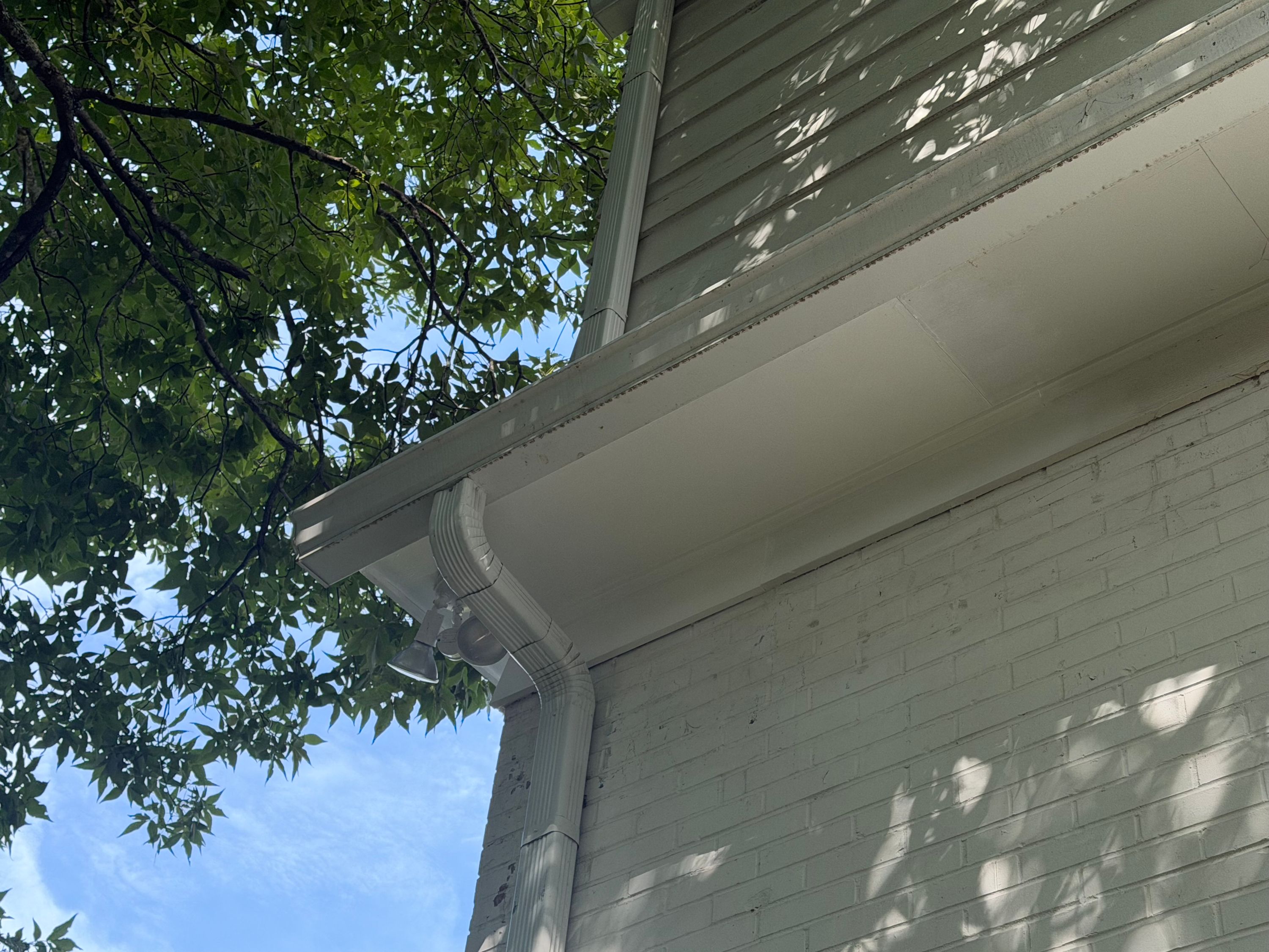 White aluminum downspouts and gutters line the painted brick siding of a two-story residence.