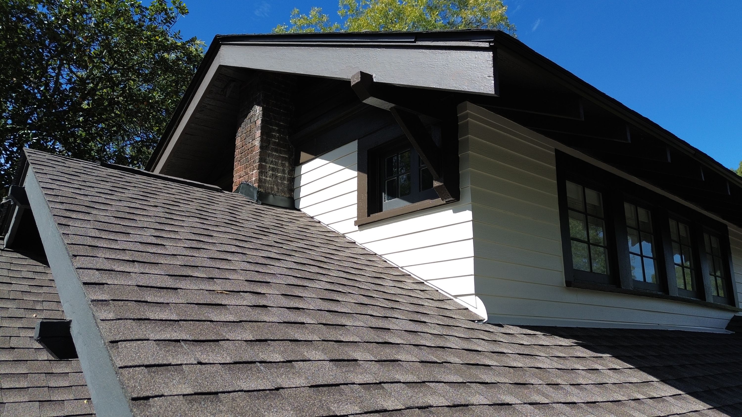 Close-up of white lap siding installation and brown architectural shingle roofing near a gable window in Birmingham.