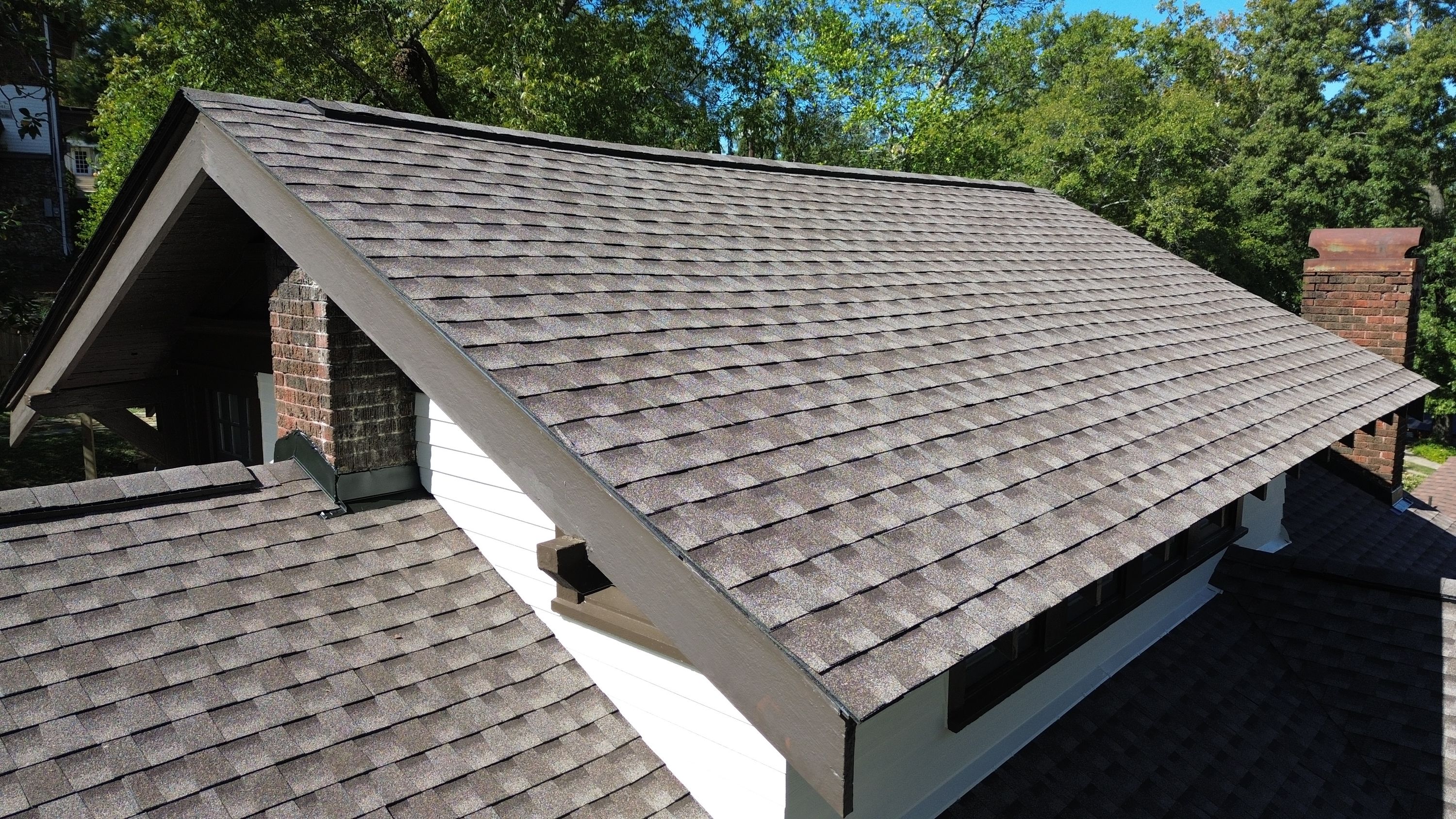 New architectural shingles meet dark brown fascia along the gable rake edge above a lower roof plane.