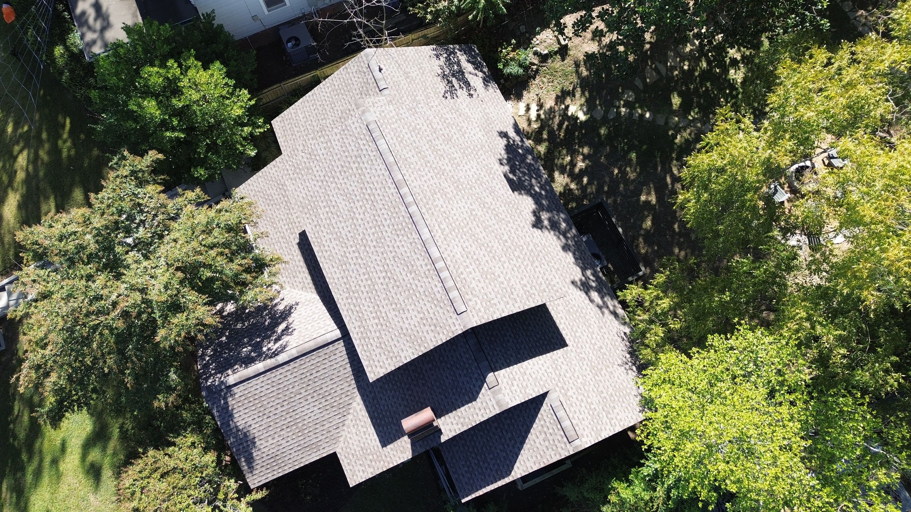 Top-down angle of new shingle roofing in Birmingham highlighting multiple ridge vents and a brick chimney.