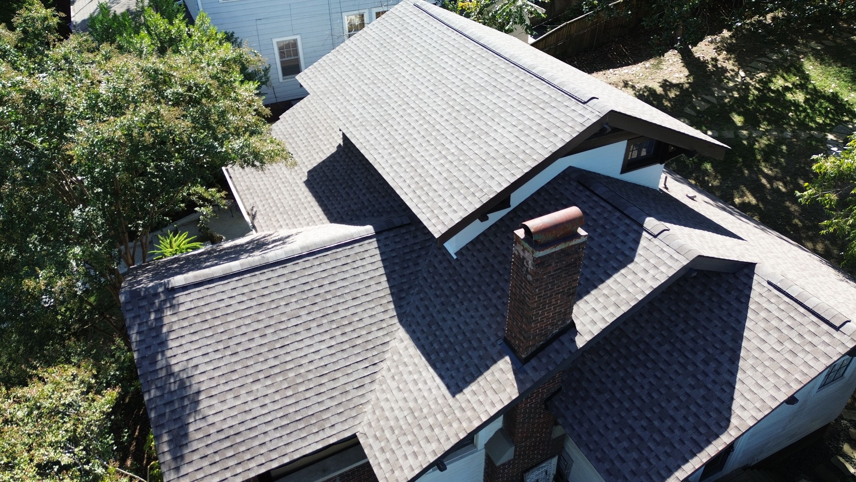 Angled aerial view of intersecting roof valleys, brick chimney flashing, and new shingle roofing in Birmingham.