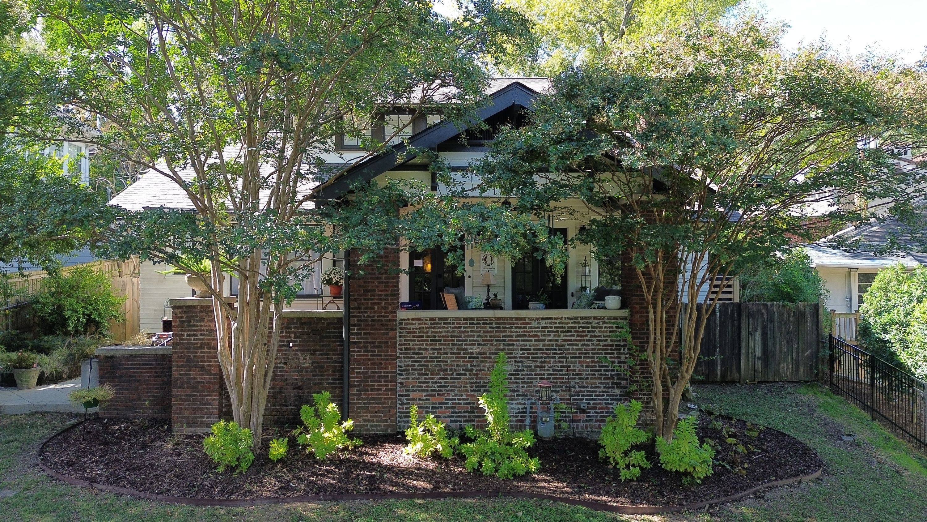 Front porch view showing dark gable trim, white siding installation, and upper shingle roofing behind brick walls.