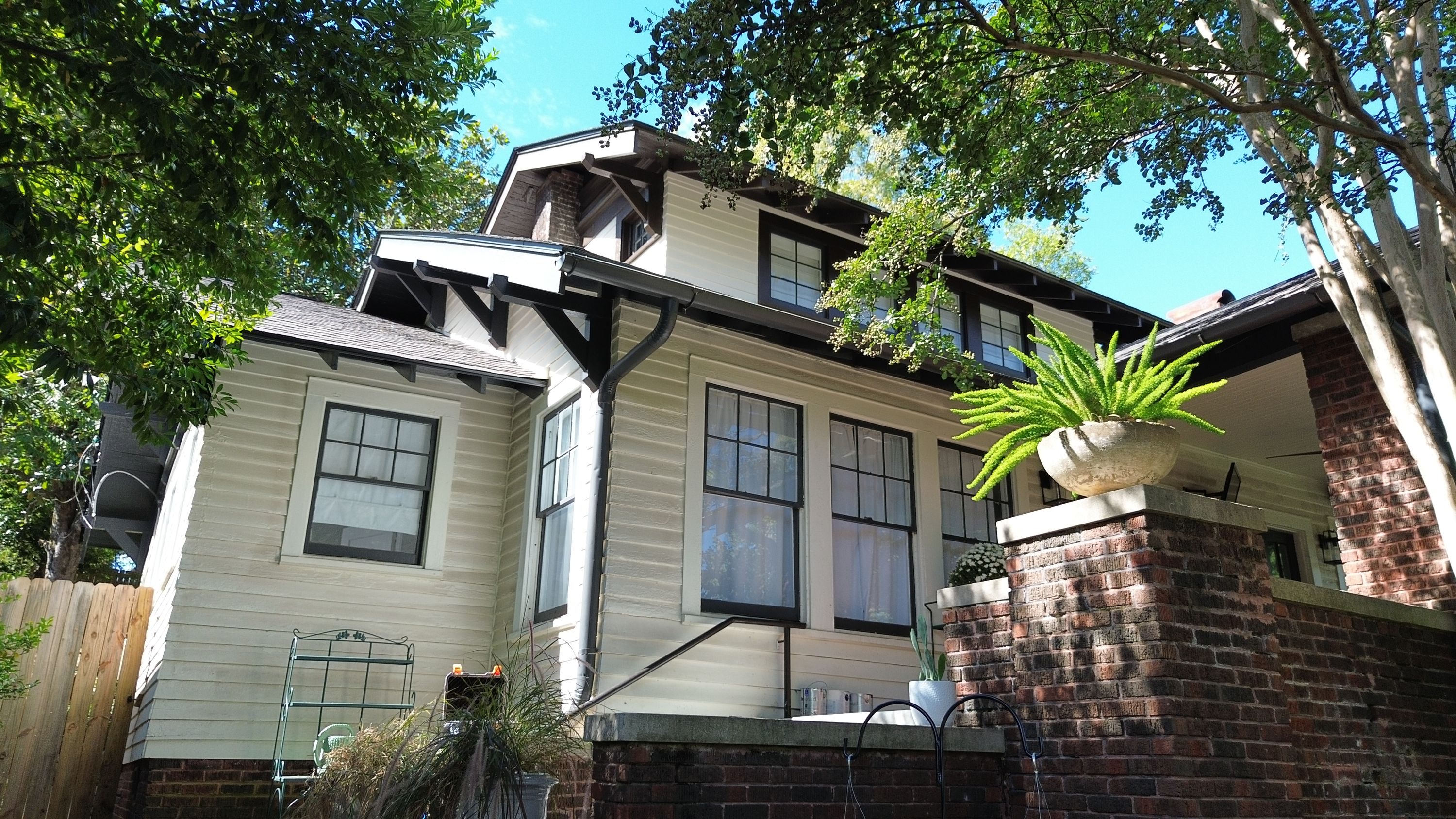 Two-story exterior corner featuring white lap siding, dark window trim, a dark downspout, and upper dormers.