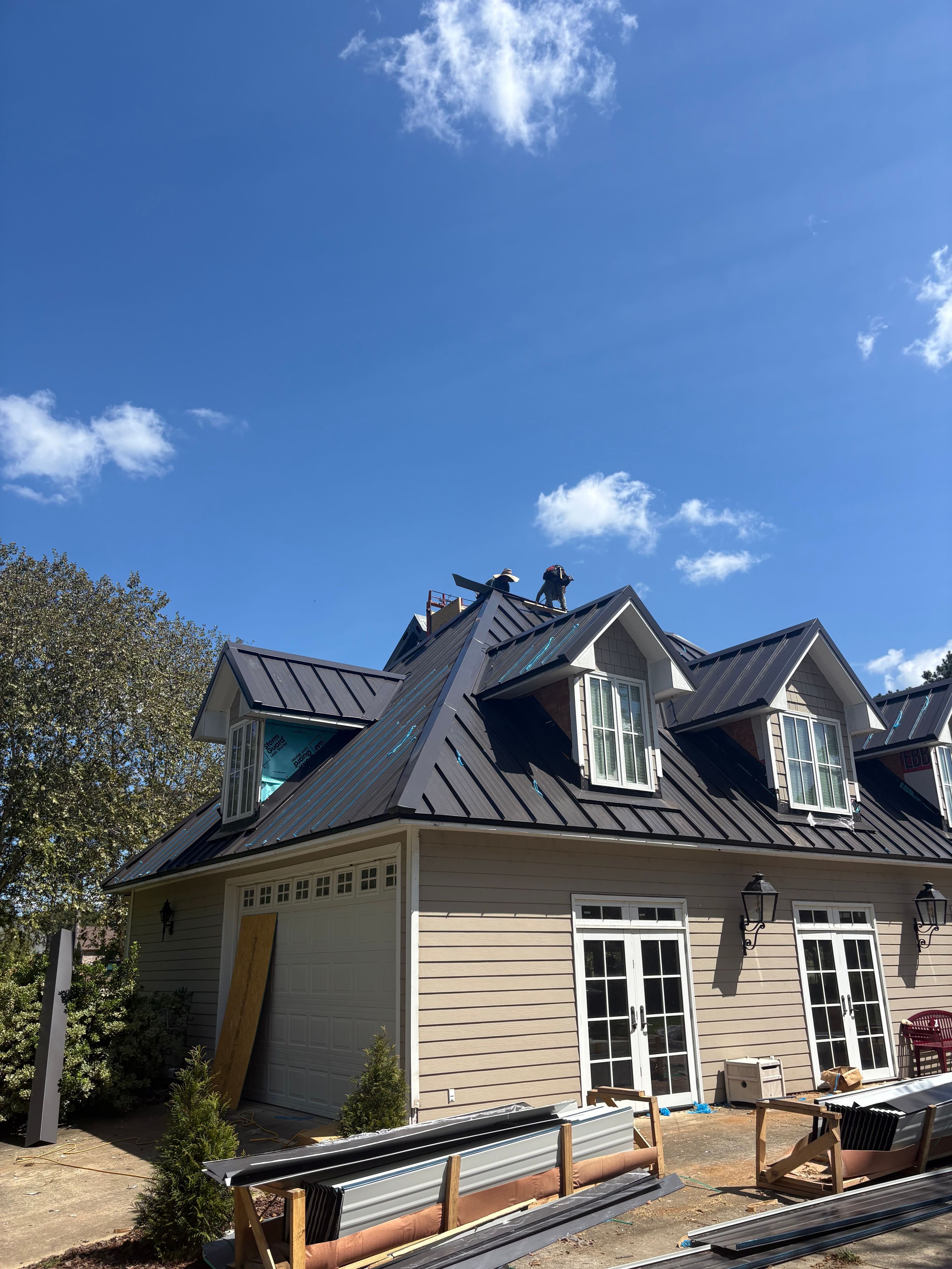 Roofers secure ridge cap flashing on a new standing seam metal roofing system in Birmingham.