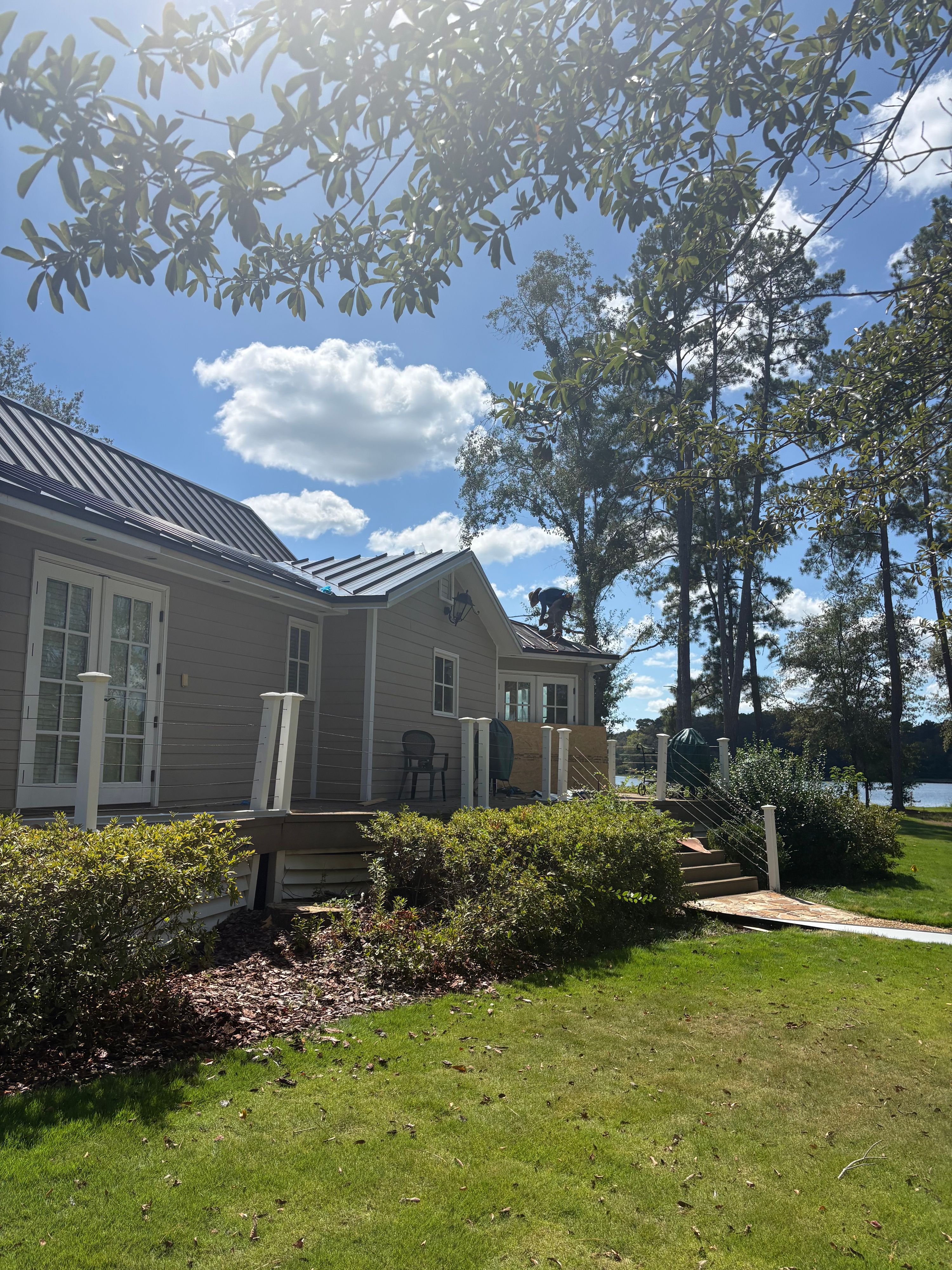 A technician installs dark standing seam metal roofing on a gabled section of a home.