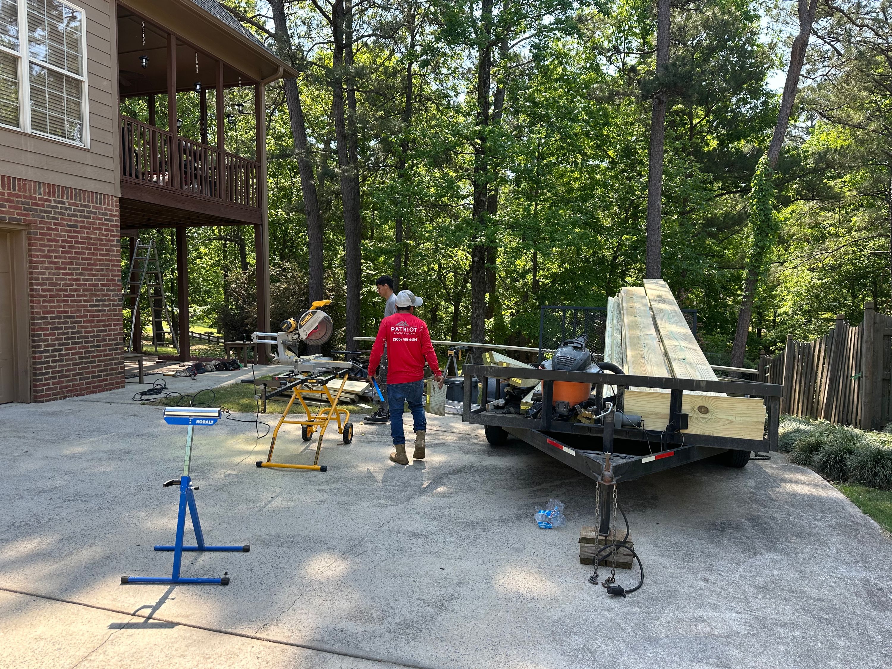 Lumber for a custom deck project sits on a trailer in a driveway in Helena alongside a miter saw on a stand.