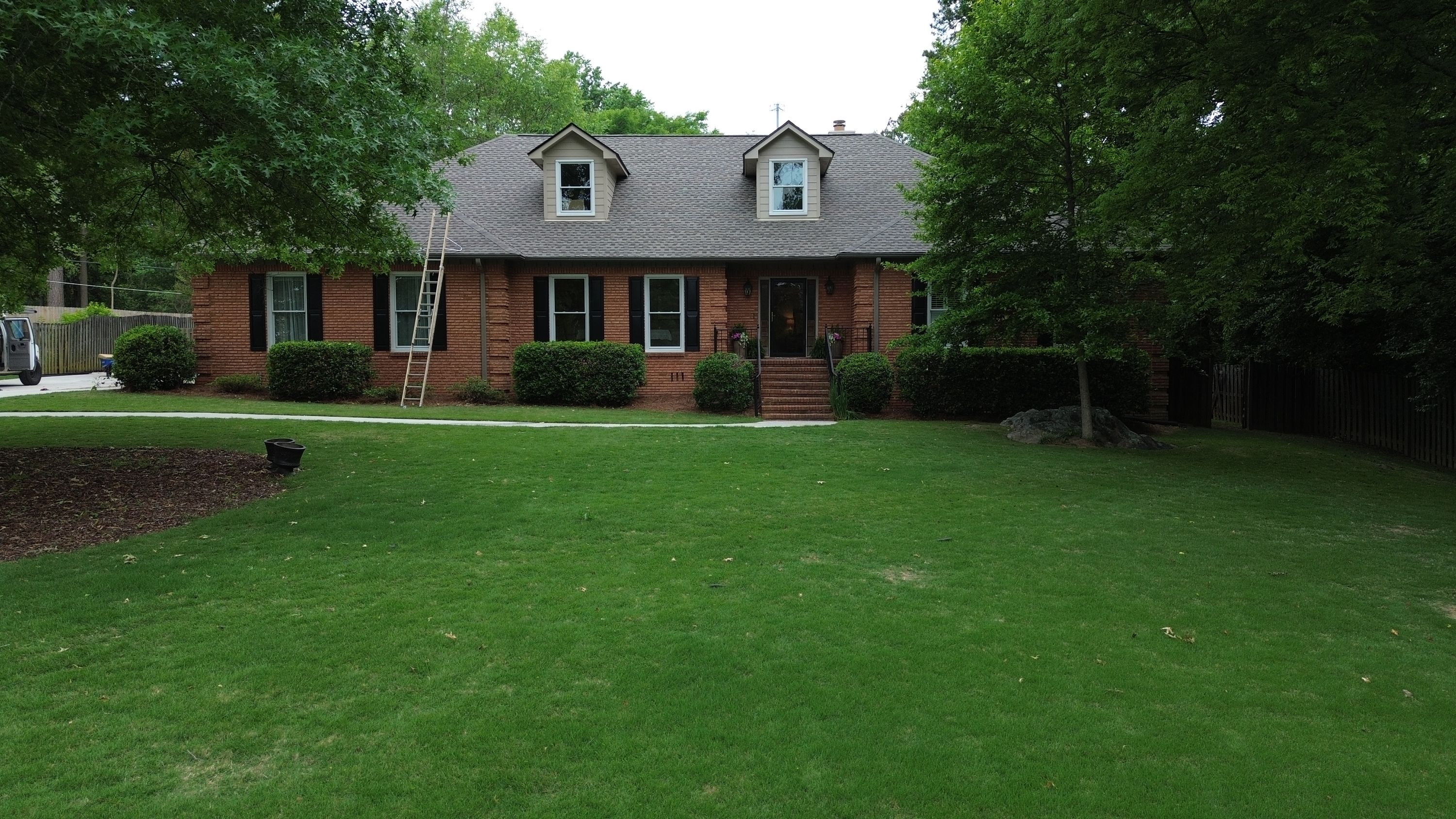 A brick home in Carisbrooke, Hoover, with a newly installed gray shingle roof and a ladder resting against the side.