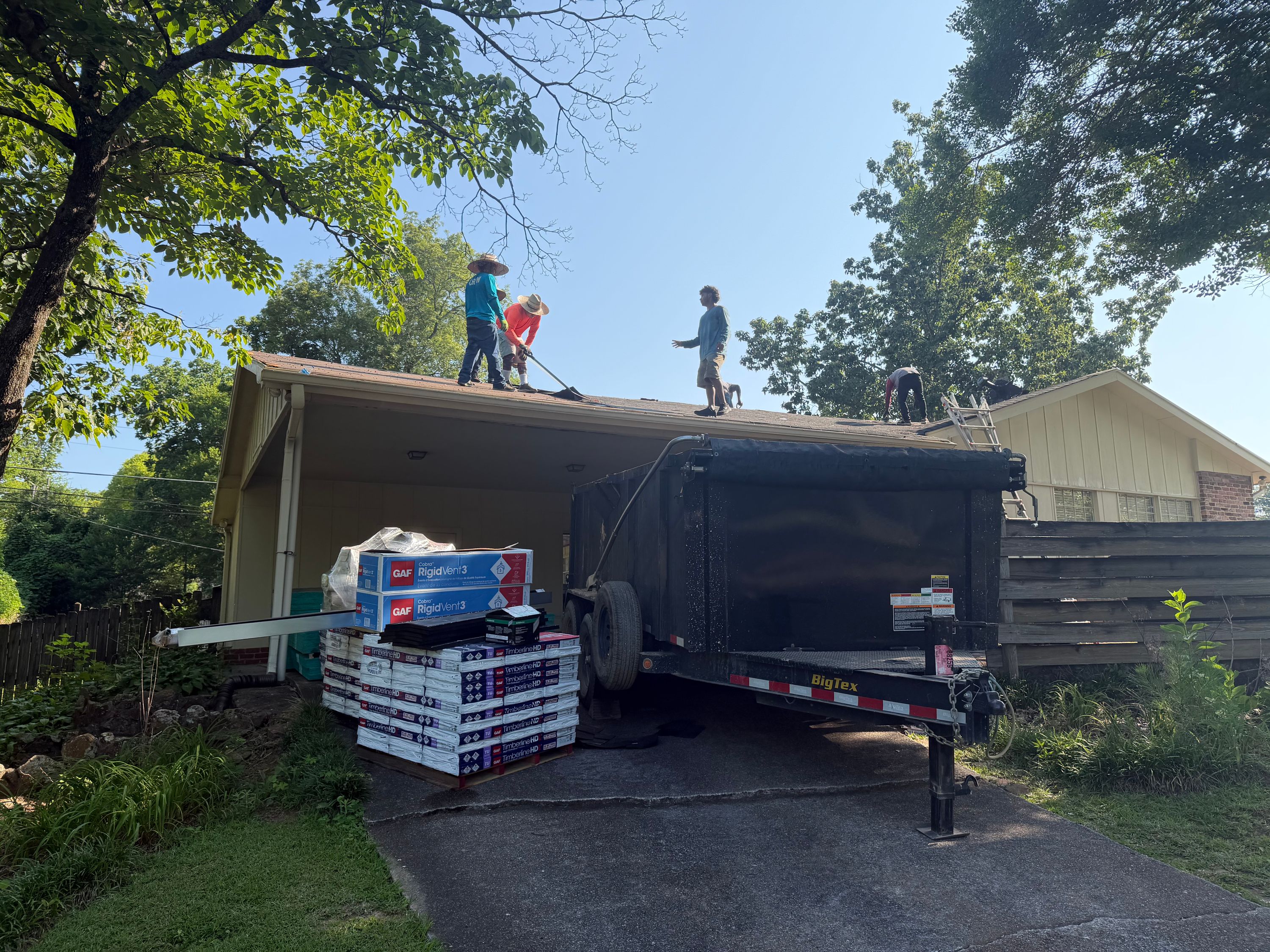 Stacked bundles of shingles sit near a large disposal trailer during a Vestavia Hills roof replacement project.
