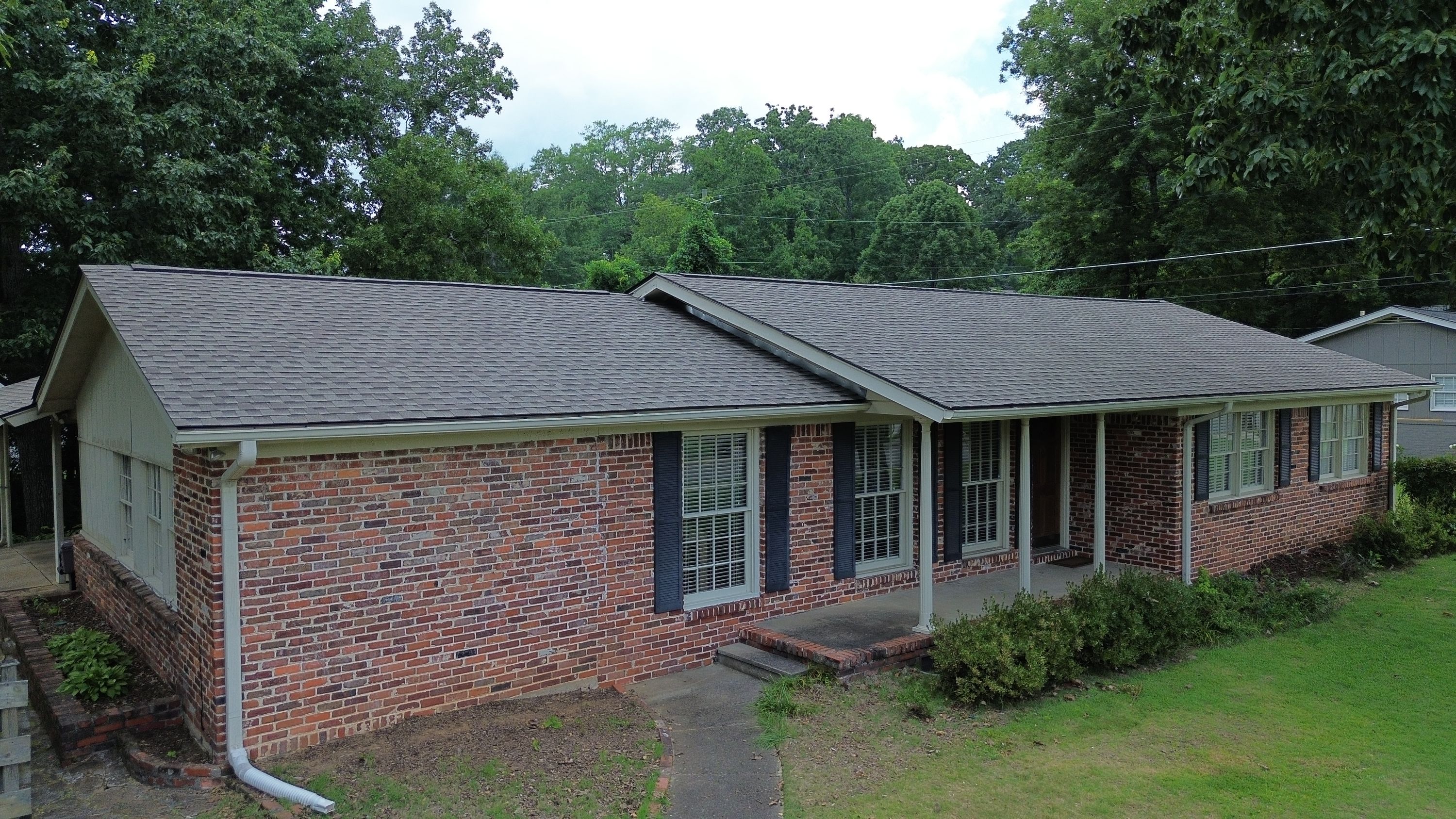 Newly installed dark grey roof shingles sit above the brick facade and black shutters of this home.