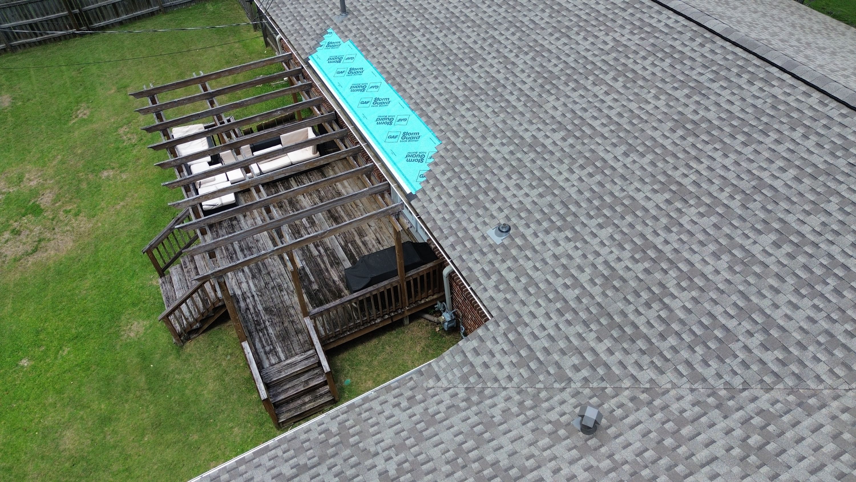 Turquoise leak barrier underlayment protects the roof edge above a weathered backyard deck in Gentilly Forest.