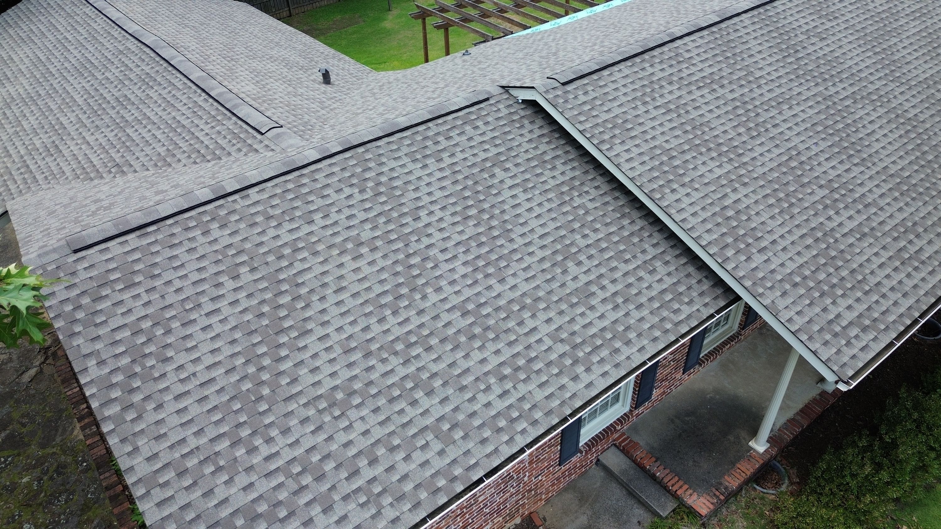 Gray architectural shingles cover a newly finished residential roof plane near a backyard wood pergola.
