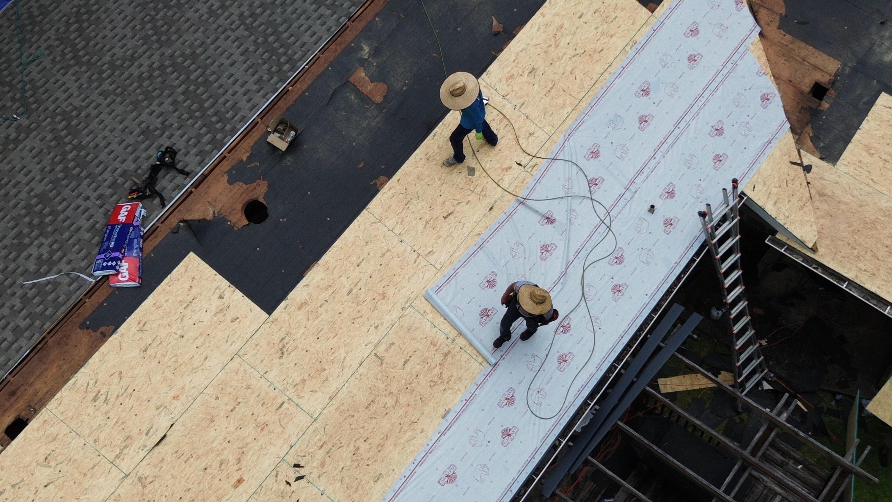 Protective white underlayment is rolled across newly installed plywood roof decking on Columbiana Road.