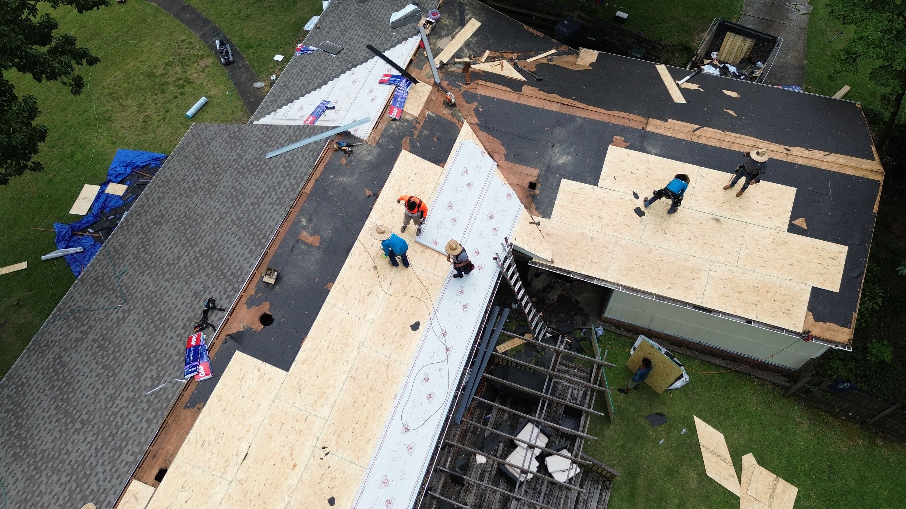 An overhead view shows white underlayment applied over new plywood decking above an exposed wooden deck frame.