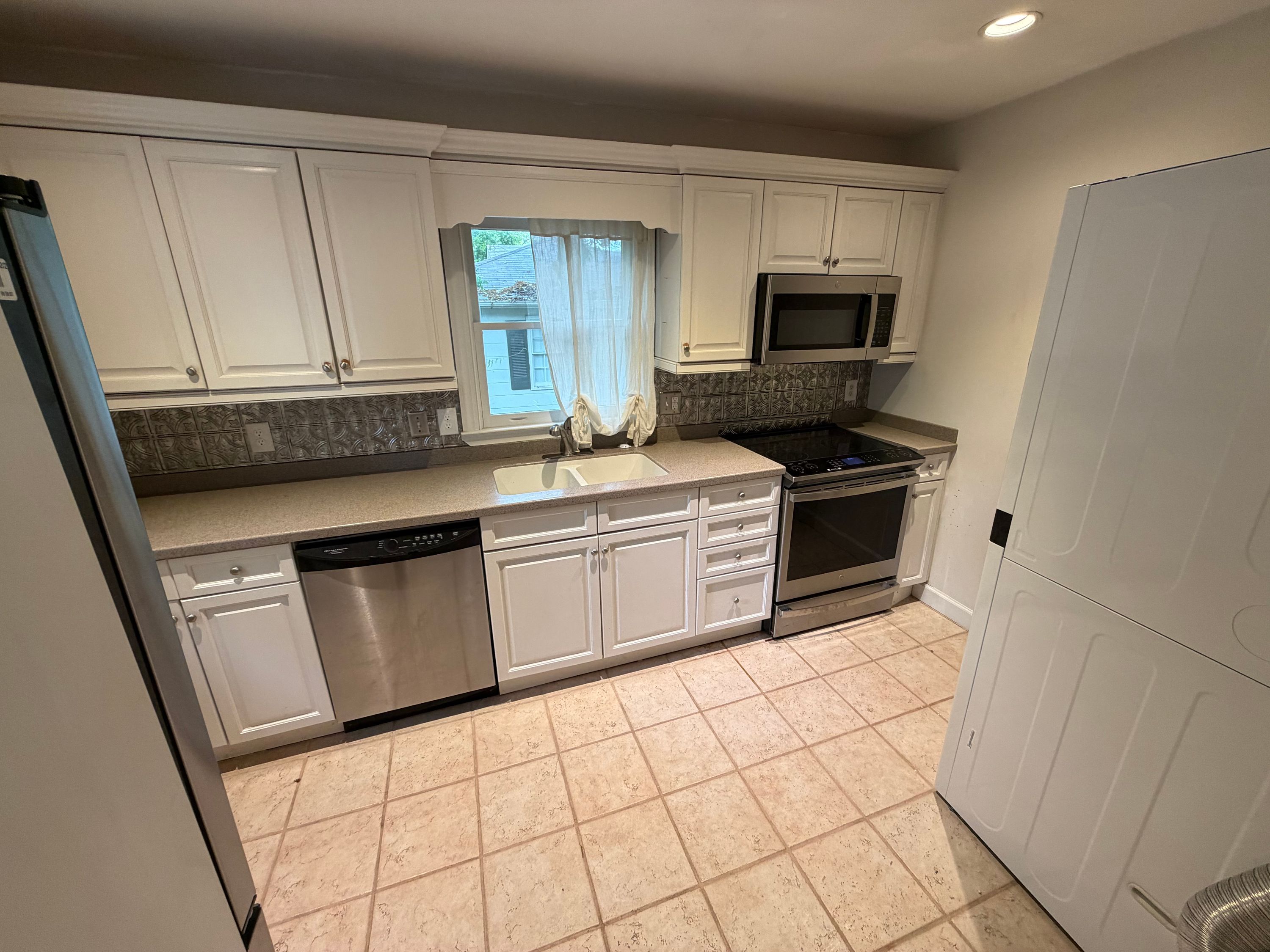 A renovated kitchen with white cabinetry, stainless steel appliances, and tiled backsplash in a West Homewood home.