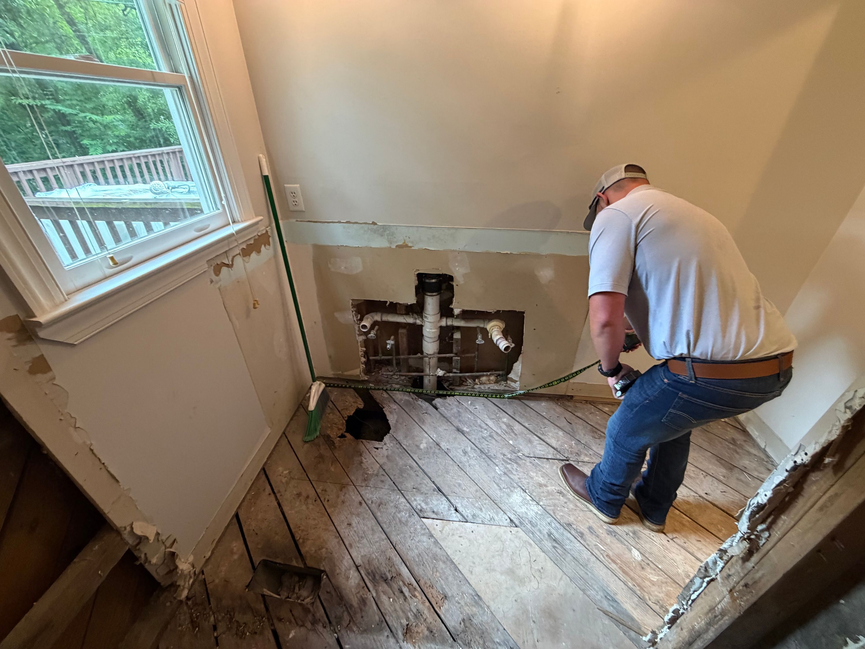 Measuring for interior renovations in a West Homewood home with exposed plumbing and damaged floorboards.