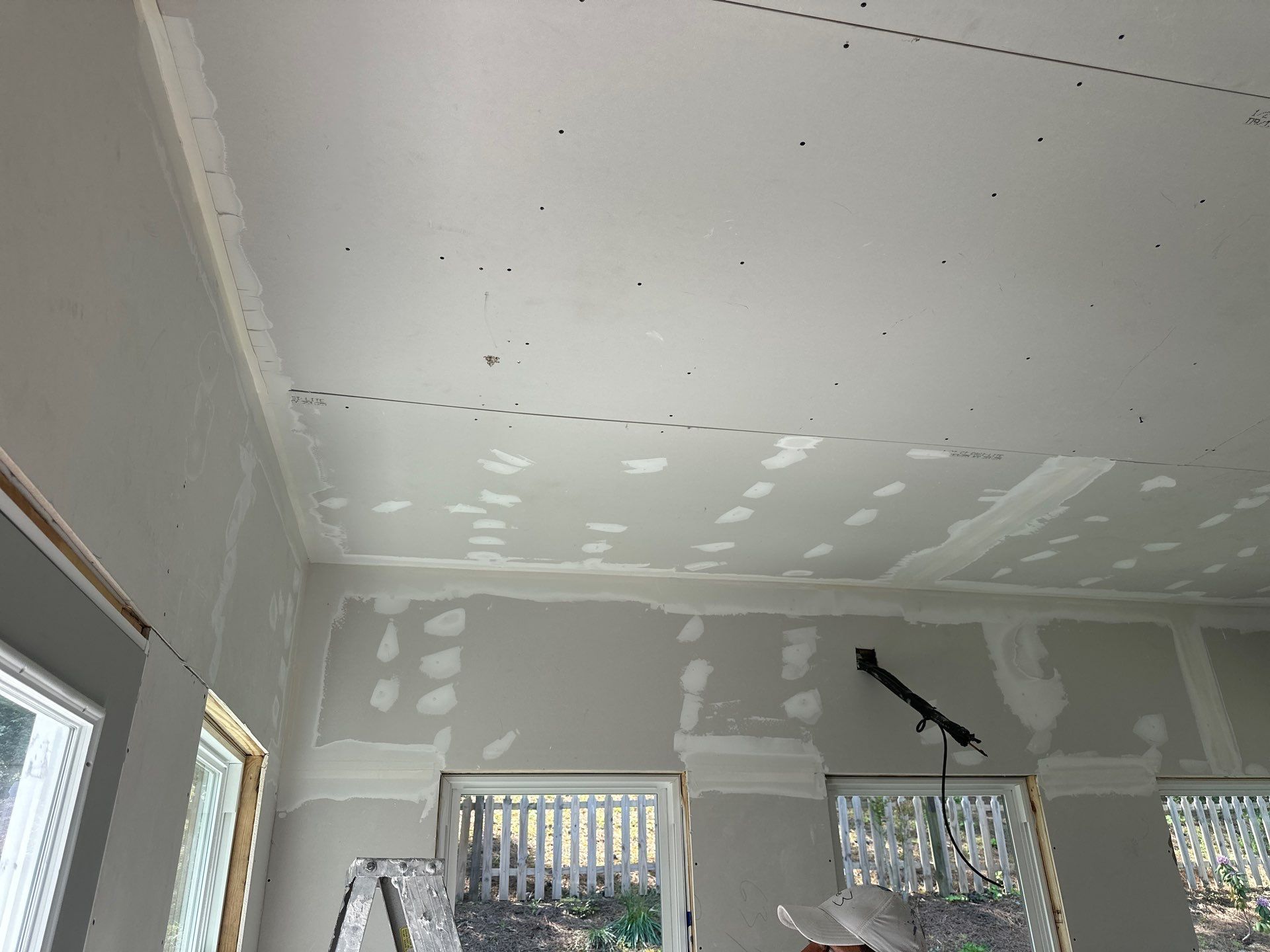 Newly installed drywall panels with mudded seams and screw heads on a ceiling and wall in a Greystone home.