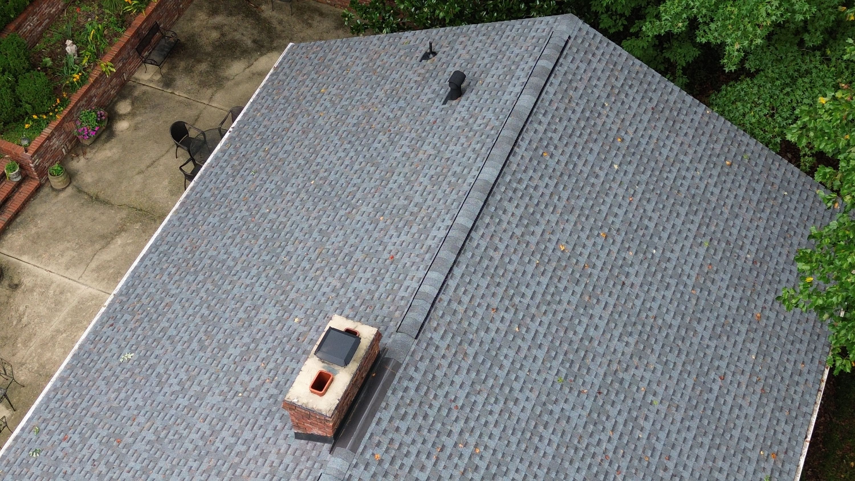 Fresh black flashing around a brick chimney next to a new ridge vent and pipe boot.