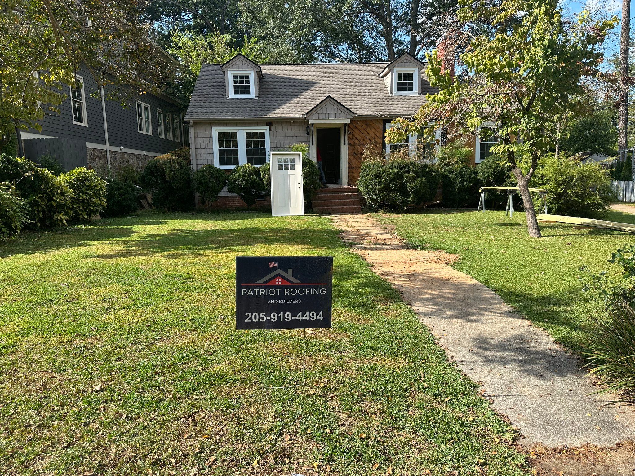 Patriot Roofing and Builders company sign in front of a window replacement project in Edgewood, Homewood.