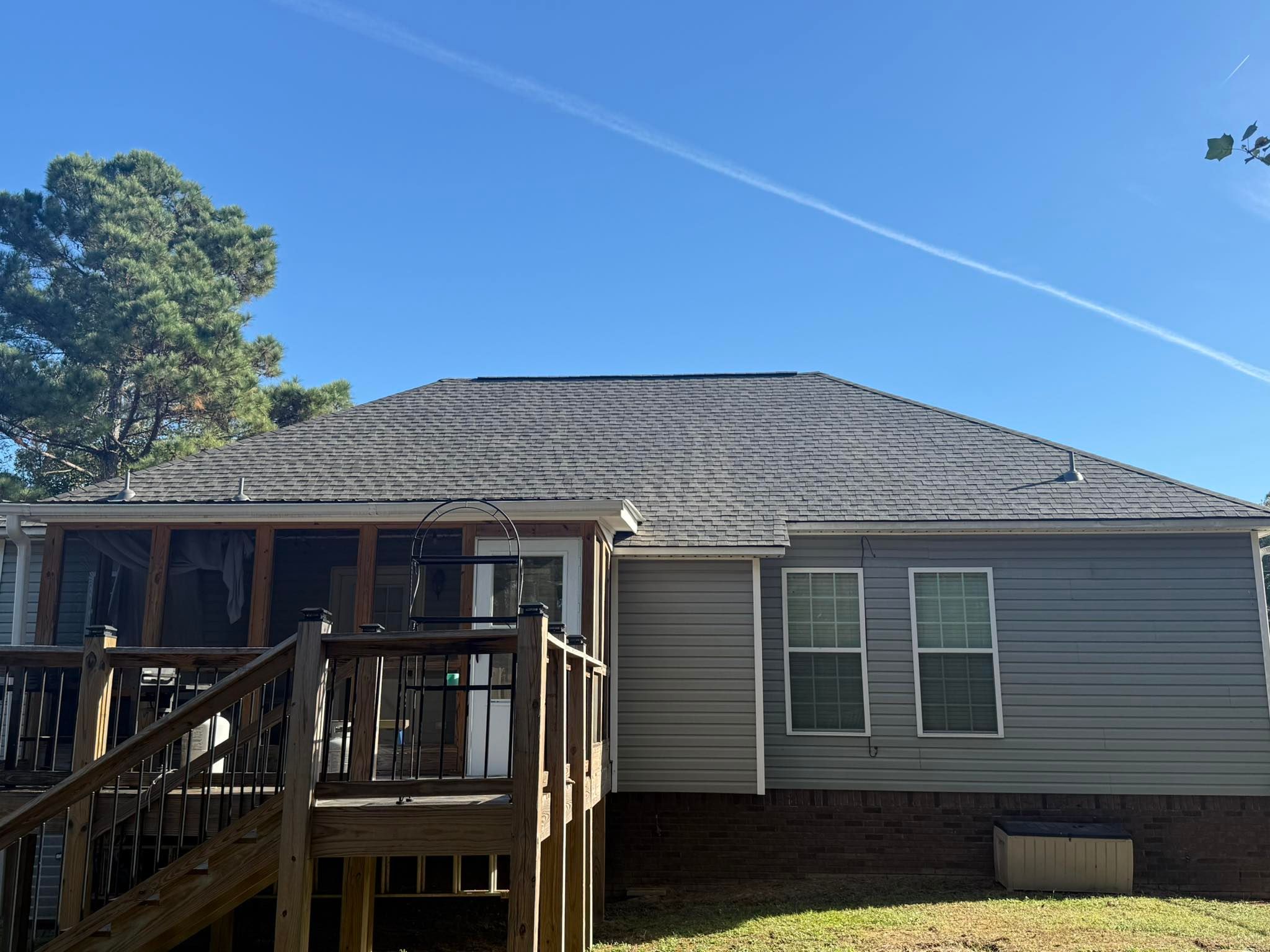 Rear view of a professional roof replacement showing new shingles and a wooden deck in Trussville, Alabama.