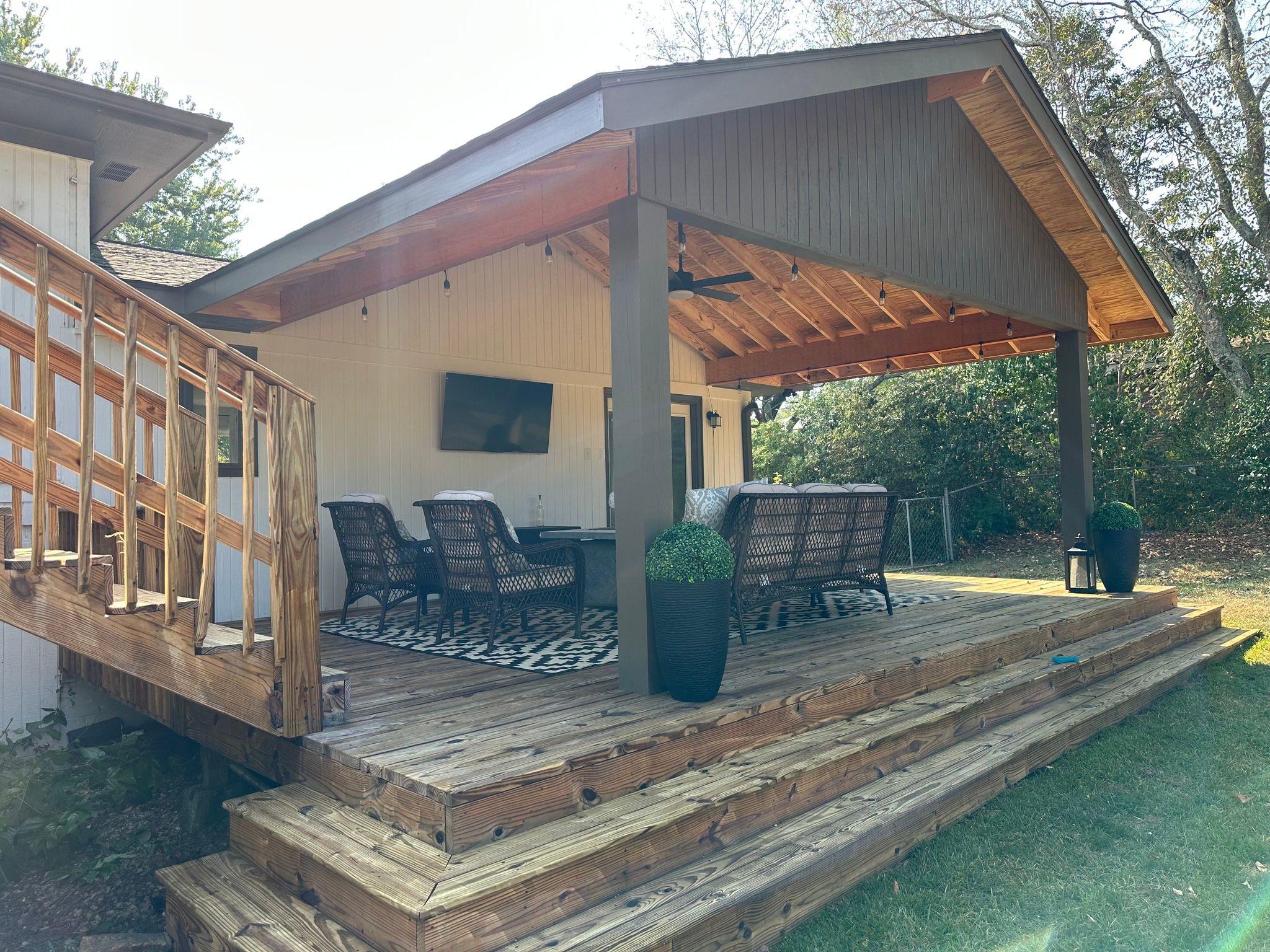 Side view of a completed custom covered deck in Hoover, AL, featuring wrap-around wooden stairs and a wall-mounted outdoor television.