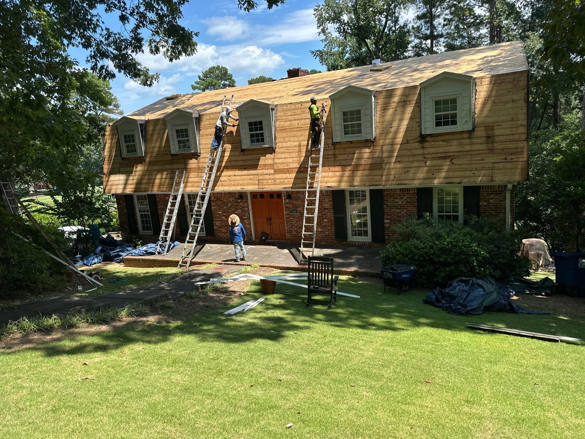Roofing crew performing a roof replacement in Hoover, Alabama, showing the exposed decking on a steep gambrel roof with dormers.